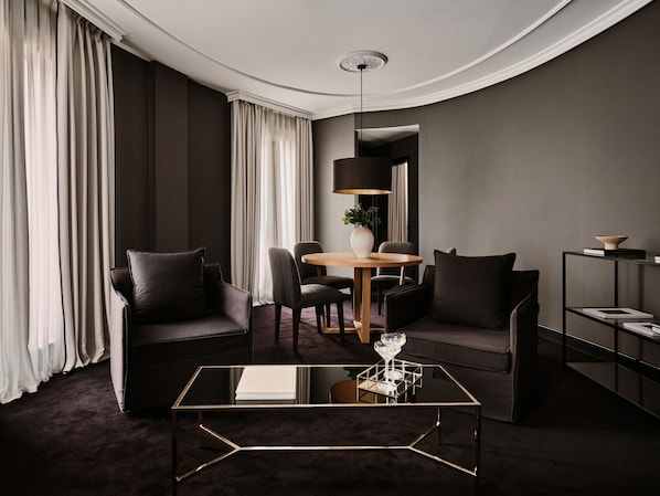 A modern hotel room with a dark color scheme, featuring a round dining table, two sofas, a glass coffee table, and a bookshelf. - The Principal Madrid, Small Luxury Hotels (Madrid)