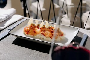 A rectangular plate with a food item, possibly sushi, garnished with green herbs and thin crackers, on a table with a white napkin and a black napkin holder.