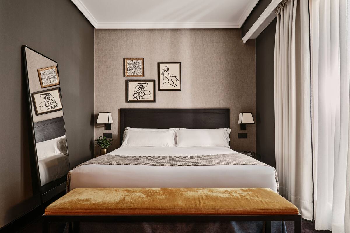 A neatly arranged hotel room with a large bed, bedside lamps, a bedside table with a plant, and framed artwork on the wall.