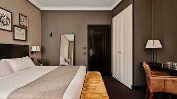 Une chambre d’hôtel avec un grand lit, un banc, un bureau avec une chaise, un miroir et des œuvres d’art encadrées accrochées au mur.