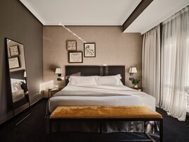 Ein Hotelzimmer mit einem großen Bett, zwei Nachttischen mit Lampen, einem Spiegel und einem Kunstwerk an der Wand.