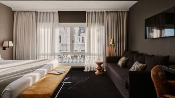 Ein Hotelzimmer mit einem Bett, einer Couch, einer Bank und einem Fernseher an der Wand.