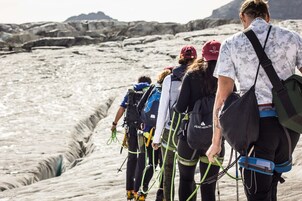 Un grupo de personas caminando sobre un glaciar con formaciones de hielo y montañas al fondo.