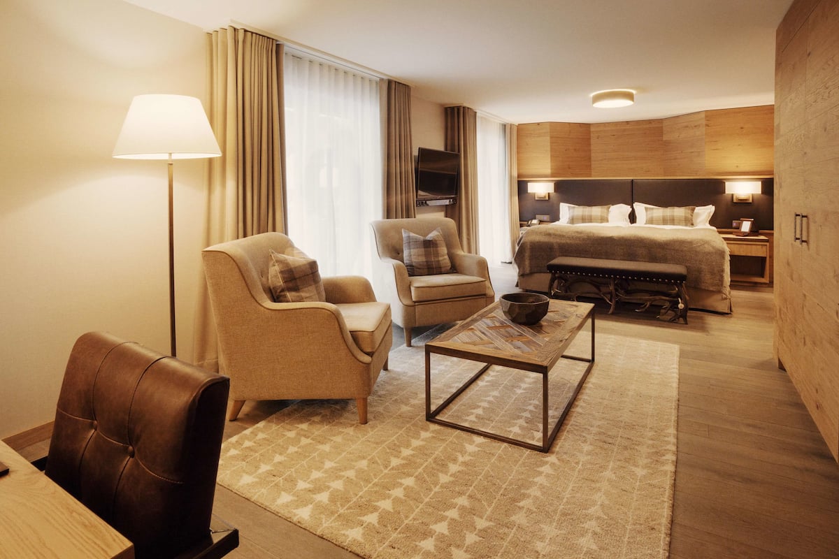 Une chambre d’hôtel équipée d’un canapé, d’un fauteuil, d’une table basse et d’un lit avec une tête de lit.