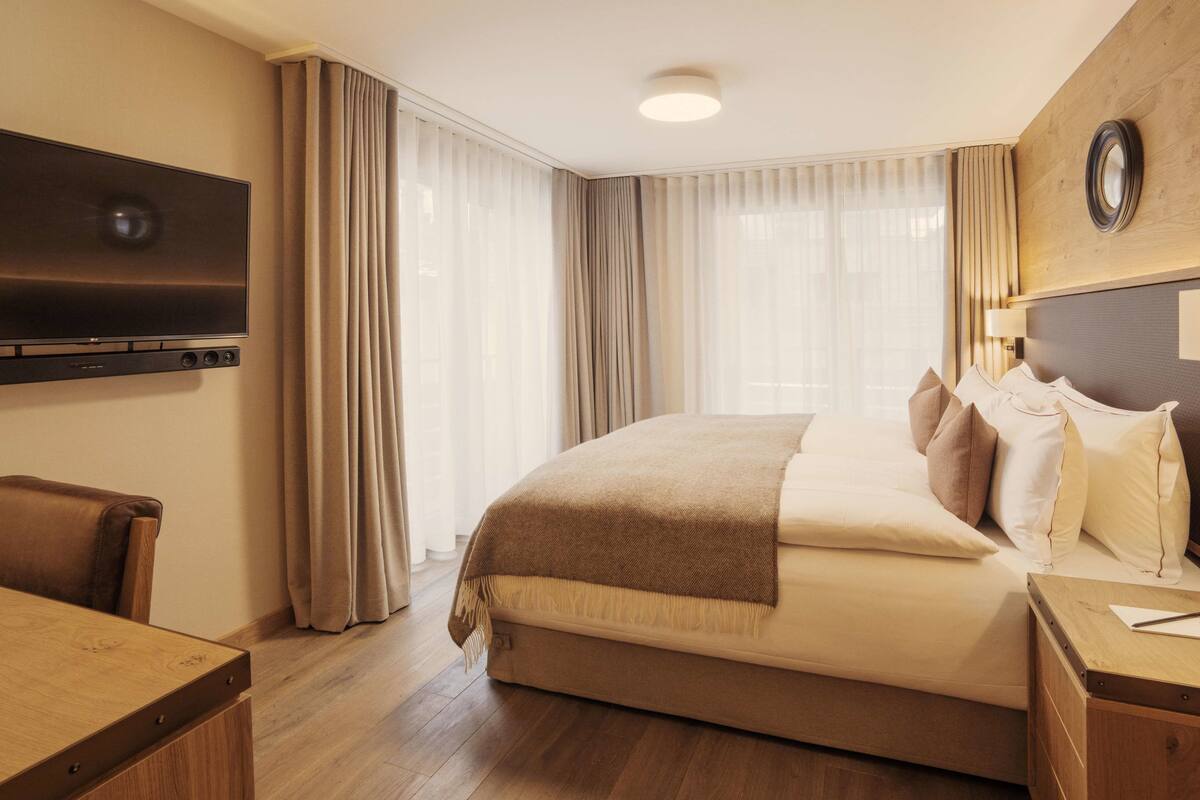 Une chambre d’hôtel avec un grand lit, un téléviseur fixé au mur, un bureau et une chaise.