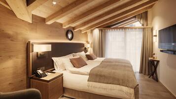 Habitación de hotel con techo de madera, una cama con ropa de cama blanca, una mesita de noche con teléfono y un televisor en la pared.