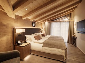 Habitación de hotel con techo de madera, una cama con ropa de cama blanca, una mesita de noche con teléfono y un televisor en la pared.