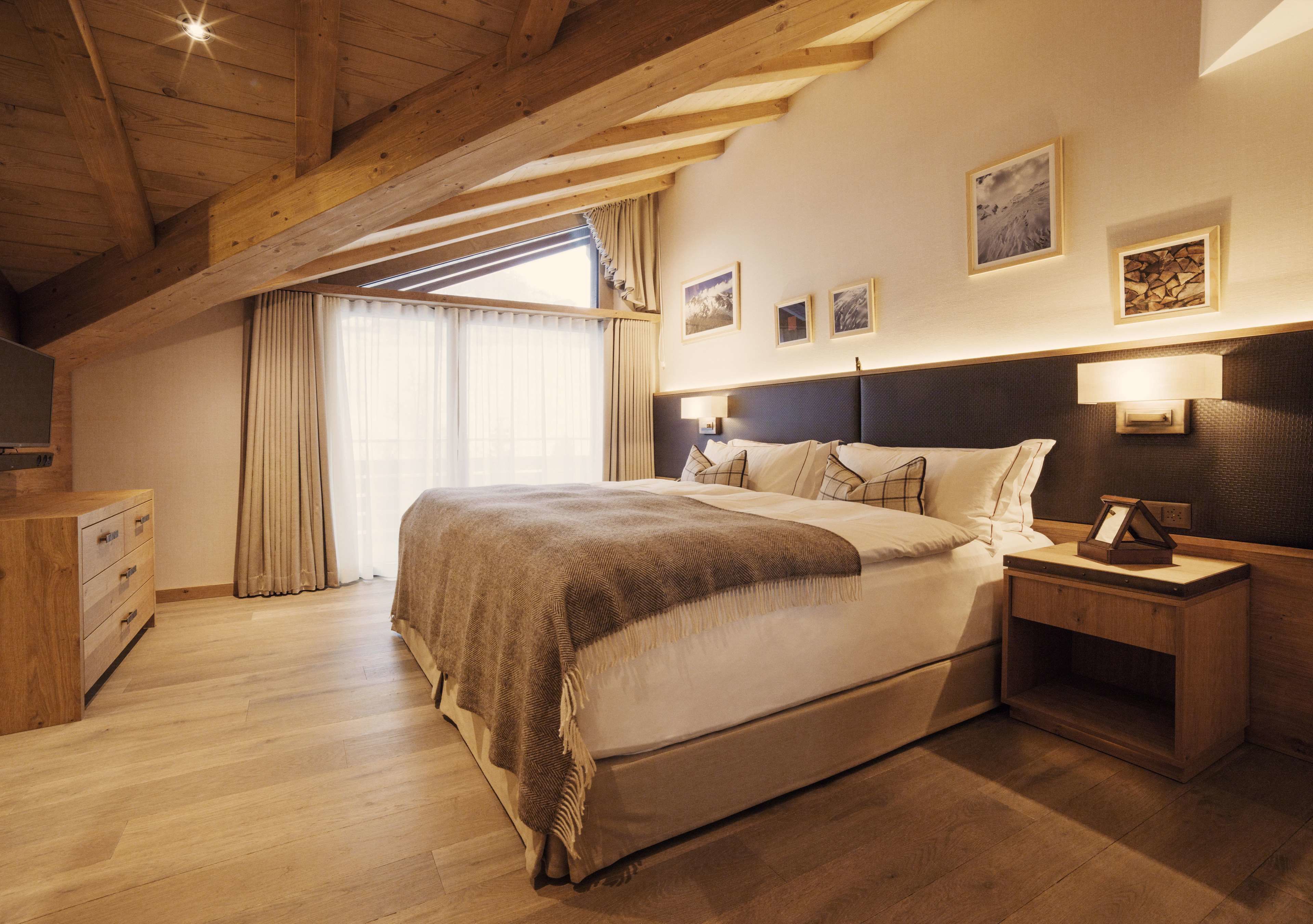 Une chambre avec un plafond en bois, un grand lit, une table de chevet et une commode.