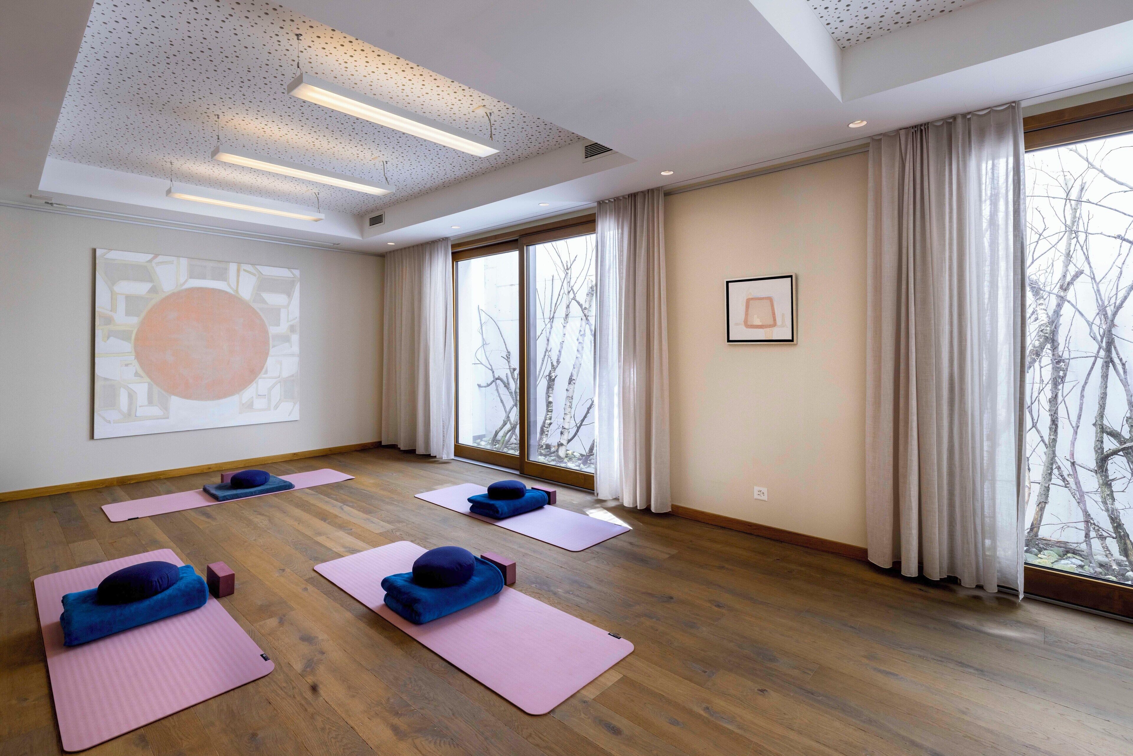A spacious room with large windows, wooden flooring, and yoga mats with blue cushions.