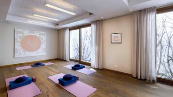 A spacious room with large windows, wooden flooring, and yoga mats with blue cushions.