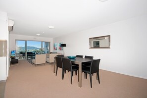 A modern dining area with a table and chairs, a large window with a view, and a mounted mirror on the wall. - Allure Hotel & Apartments (South Townsville)