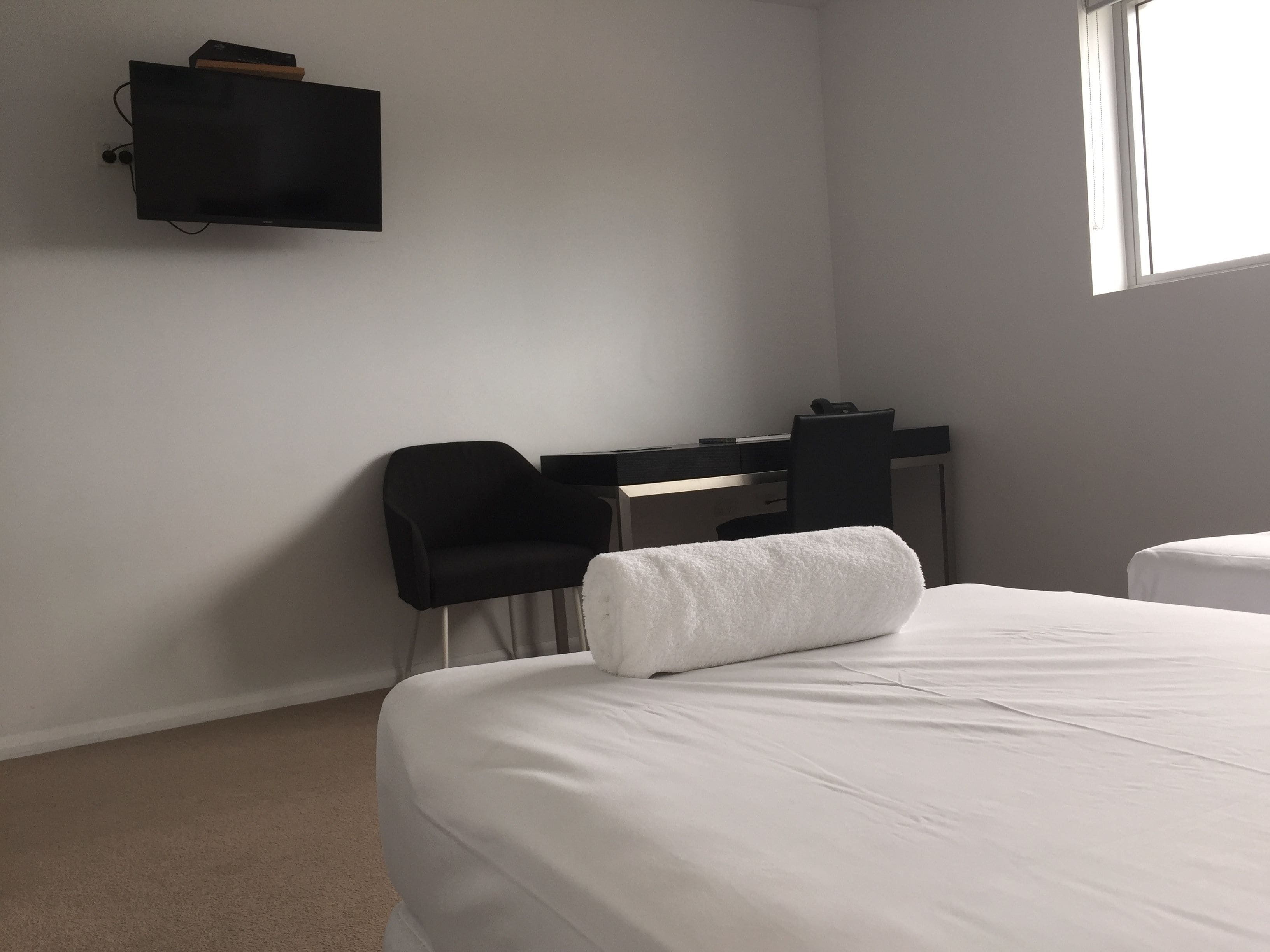 A hotel room with a bed, a desk, a chair, and a TV mounted on the wall.