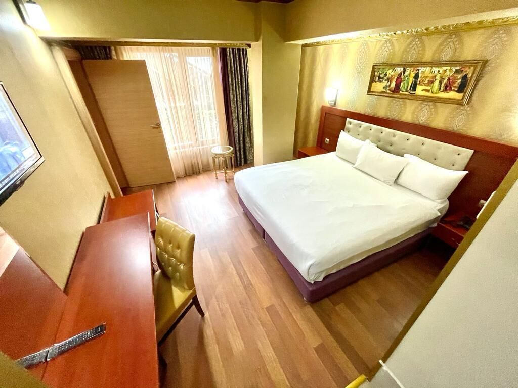 A hotel room with a large bed, a wooden desk, a chair, and a small table.