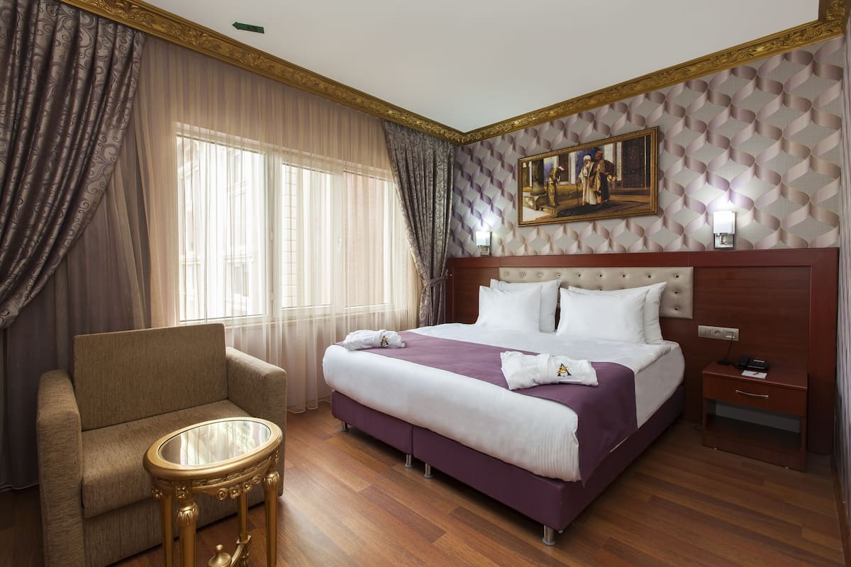 A hotel room with a large bed, a sofa, a glass table, and a painting on the wall.