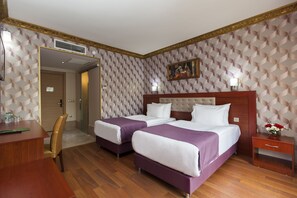 A hotel room with two beds, a wooden desk, a chair, a nightstand, and a painting on the wall.