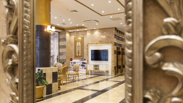 A luxurious lobby with a checkered floor, ornate furniture, a large TV, and a decorative wall.