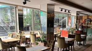 A spacious indoor area with multiple tables and chairs, large windows, and a view of the outside.