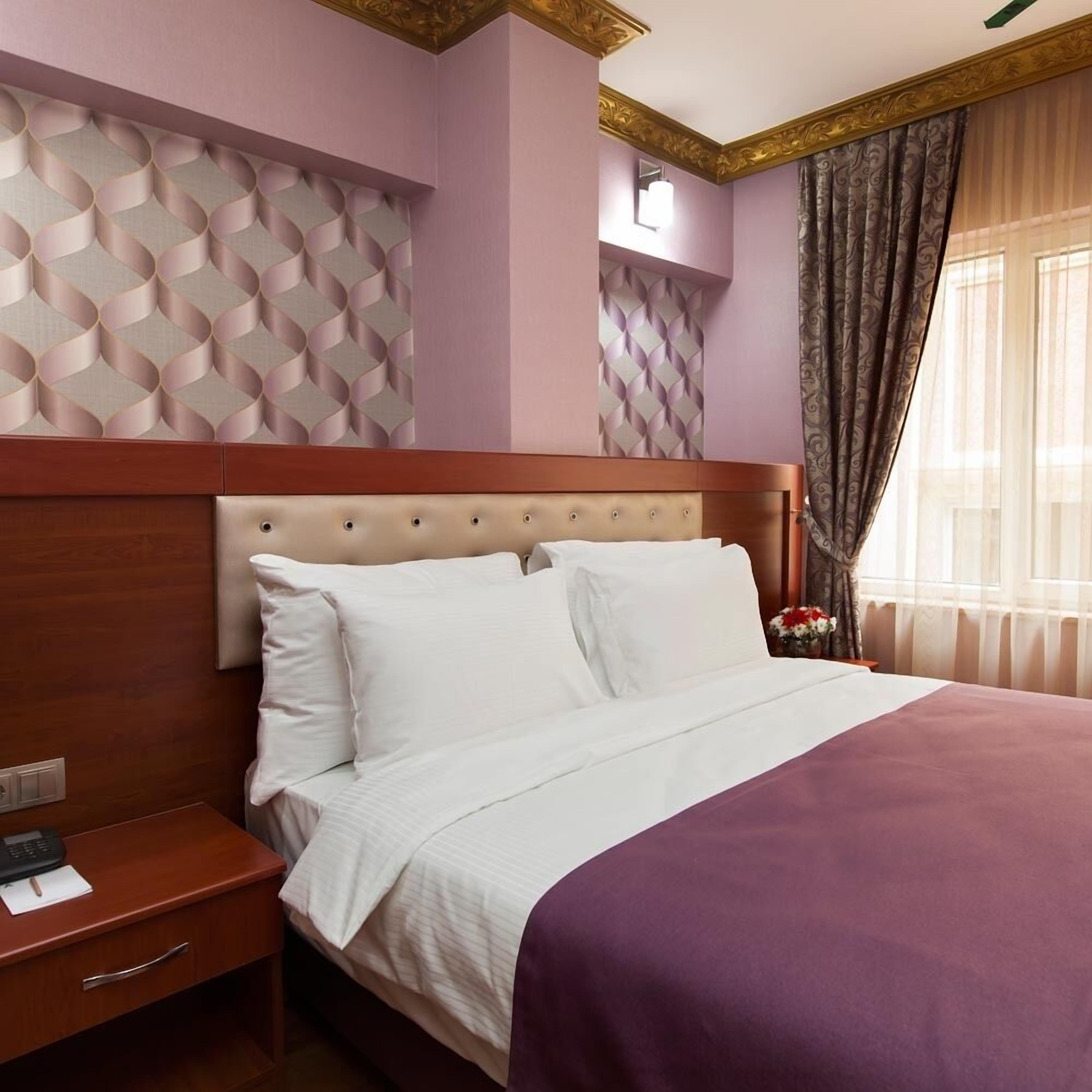 Une chambre d’hôtel avec un lit, une table de chevet, un mur orné d’un motif géométrique et une fenêtre avec des rideaux.