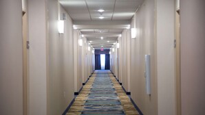 Un largo y estrecho pasillo de hotel con piso alfombrado y paredes de color claro.