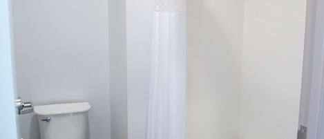 A bathroom with a toilet, a shower with a glass door, and a white curtain.