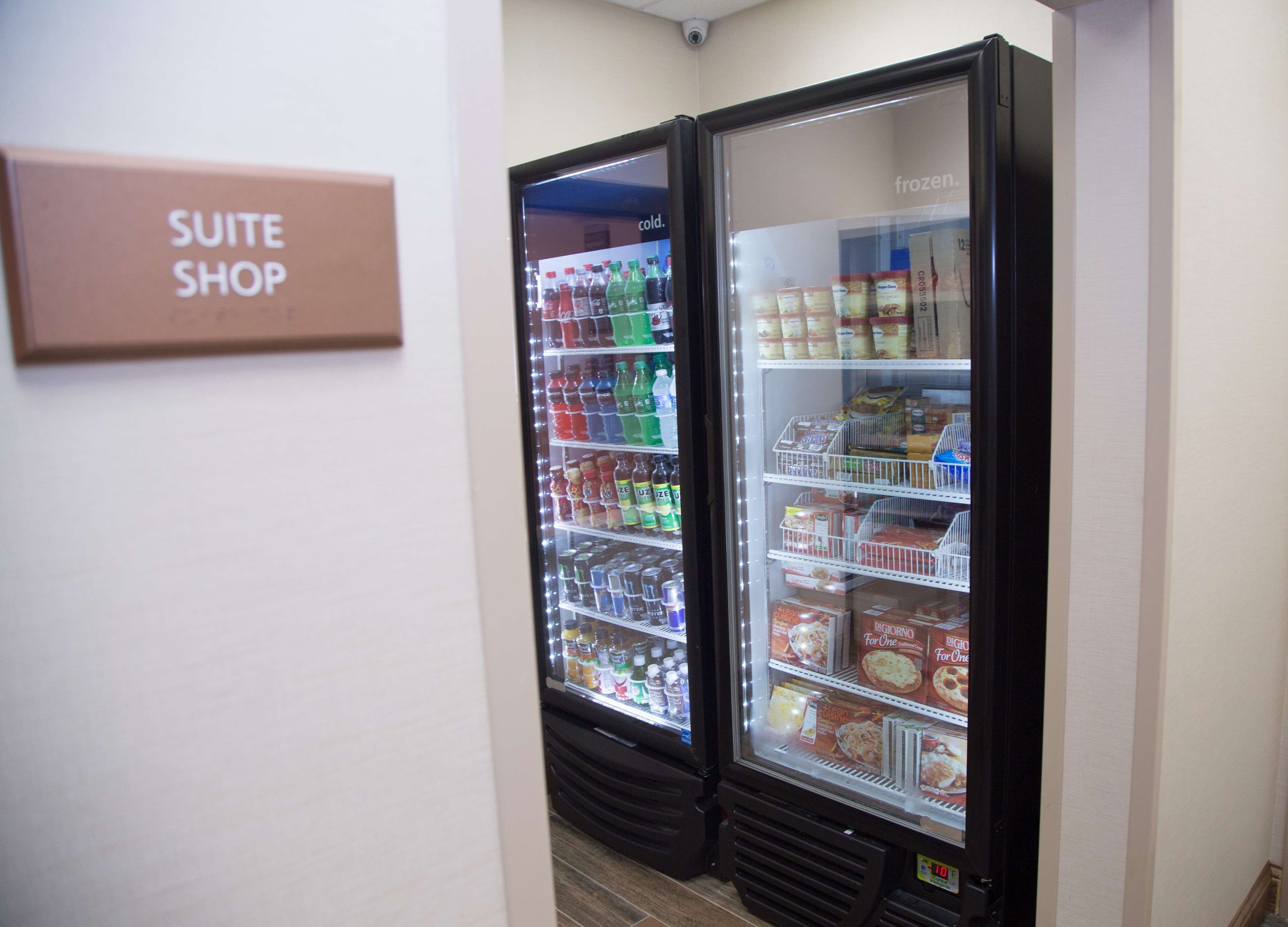 Dans un couloir, on trouve deux vitrines réfrigérées : l’une, étiquetée « SUITE SHOP », est remplie de boissons et d’en-cas, et l’autre contient des produits alimentaires surgelés.