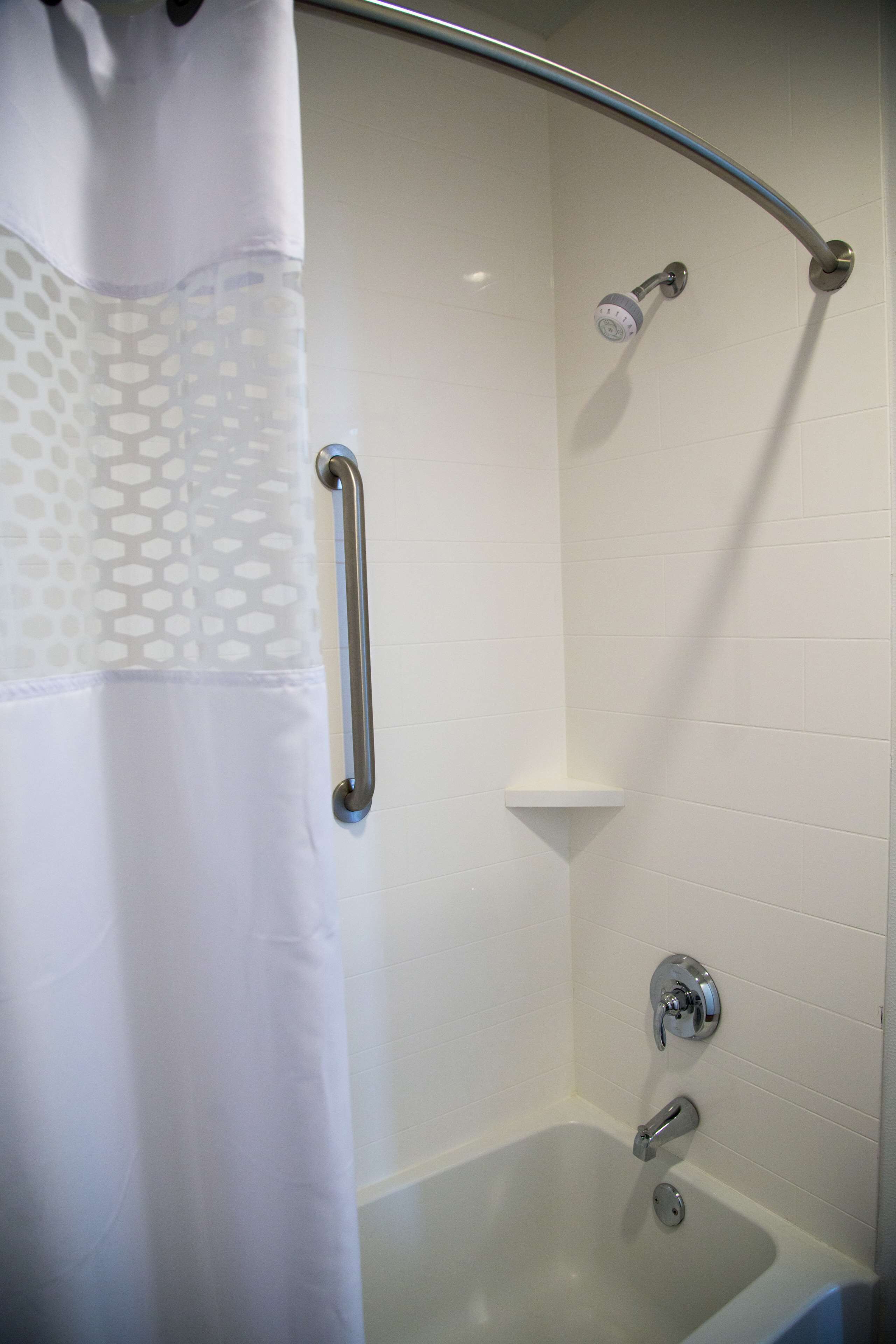 A shower area with a white tiled wall, a showerhead, a handheld shower attachment, and a grab bar.