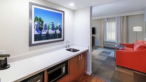 Ein modernes Hotelzimmer mit Küchenzeile, einem roten Sofa und einem an der Wand befestigten Flachbildfernseher.