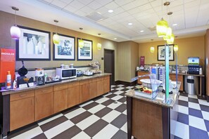 Une cuisine d’hôtel avec un carrelage à motifs, un four à micro-ondes, une machine à café et un comptoir de buffet proposant divers plats.