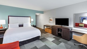 Ein Hotelzimmer mit einem großen Bett, einem Schreibtisch mit Fernseher, einem Sessel und einem kleinen Tisch.