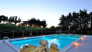 A swimming pool with a stone sculpture in the foreground, surrounded by a fence and trees. - Agriturismo Antico Podere Siliano (Citta della Pieve)