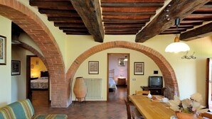 A cozy living room with a wooden dining table, a sofa, and a TV. - Agriturismo Antico Podere Siliano (Citta della Pieve)