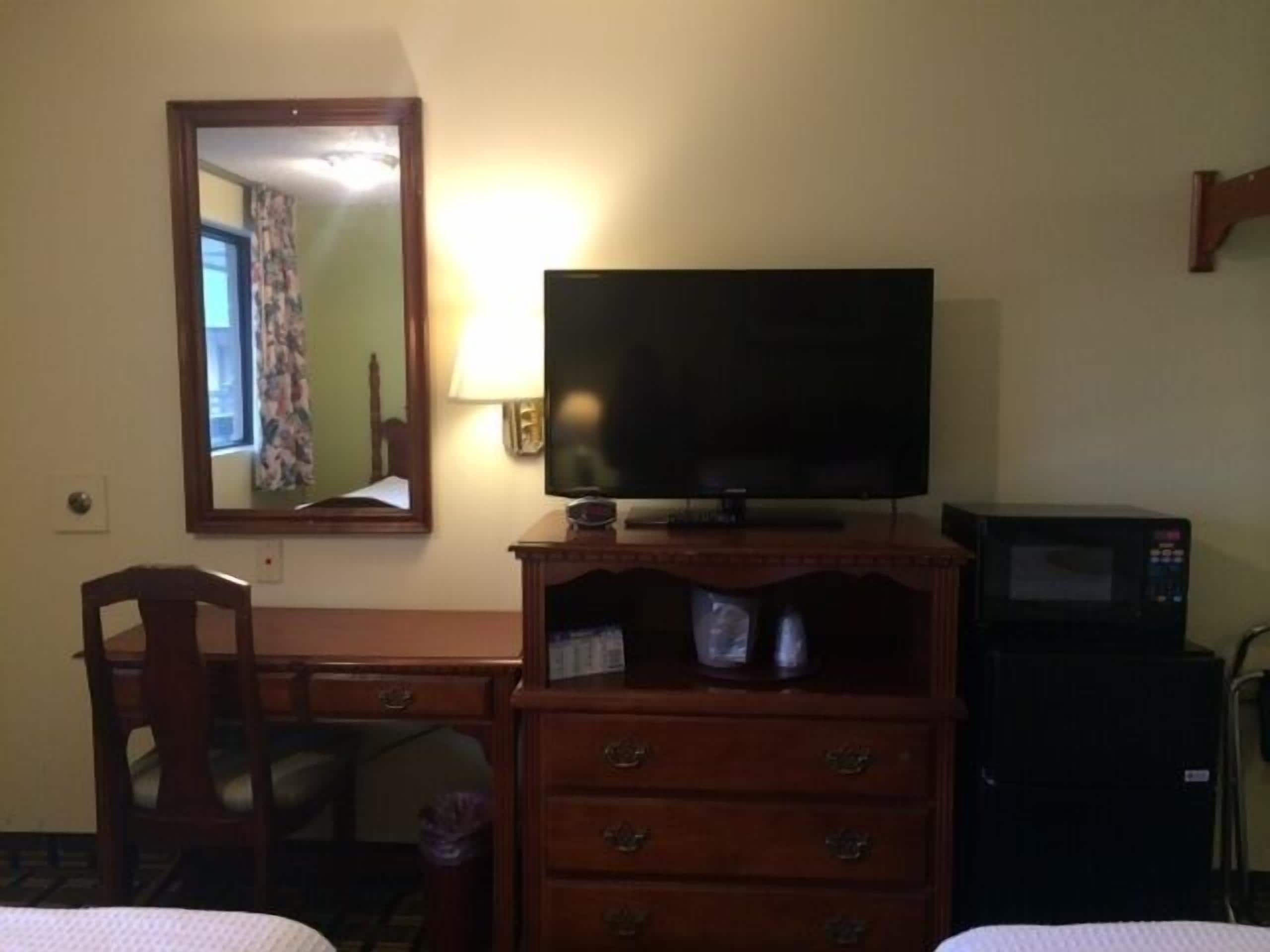A hotel room with a wooden dresser, a television, a microwave, and a chair.