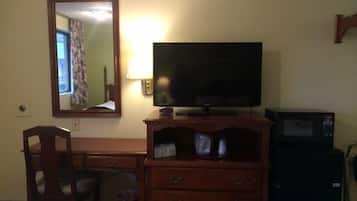 A hotel room with a wooden dresser, a television, a microwave, and a chair.