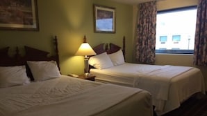 A hotel room with two single beds, a nightstand with a lamp, and a window with curtains.