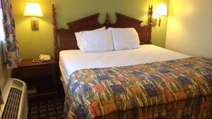 A hotel room with a wooden headboard, two bedside lamps, a telephone, and a colorful quilt.