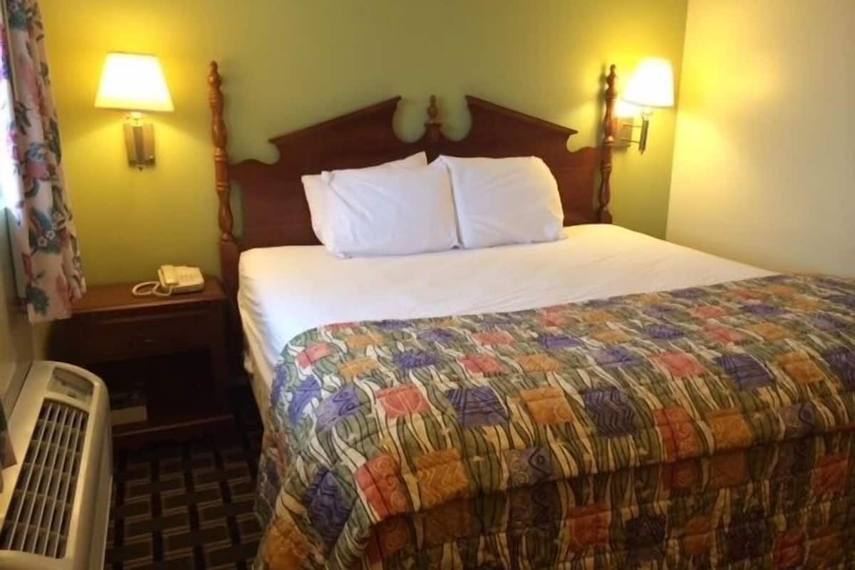 A hotel room with a wooden headboard, two bedside lamps, a telephone, and a colorful quilt.