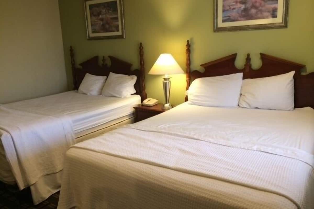A hotel room with two single beds, a bedside table with a lamp, and a painting on the wall.