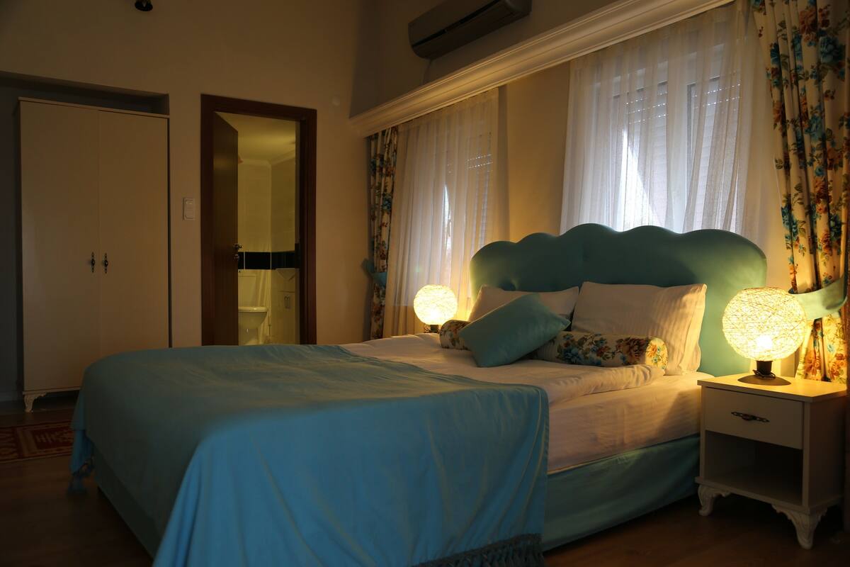 Un dormitorio con cama, mesitas de noche, un espejo y cortinas.