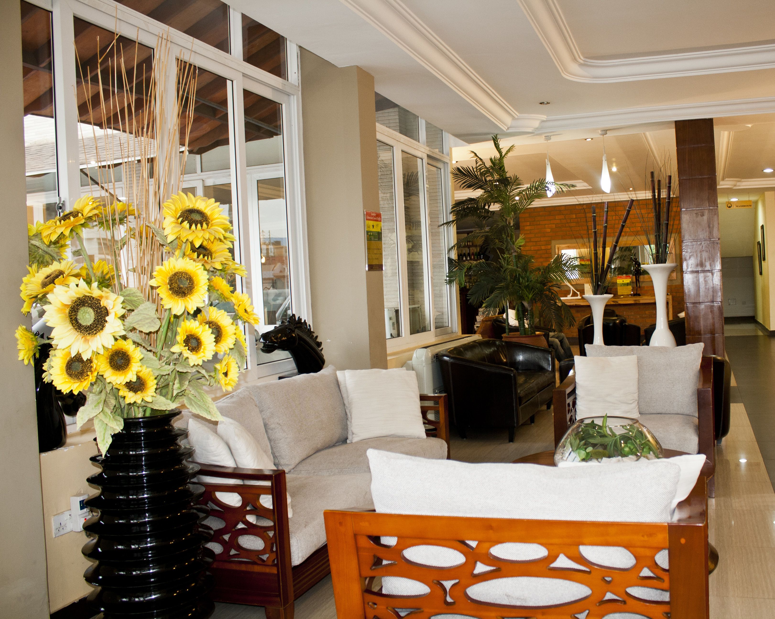 A spacious lobby with a sofa, chairs, and a large vase of sunflowers.