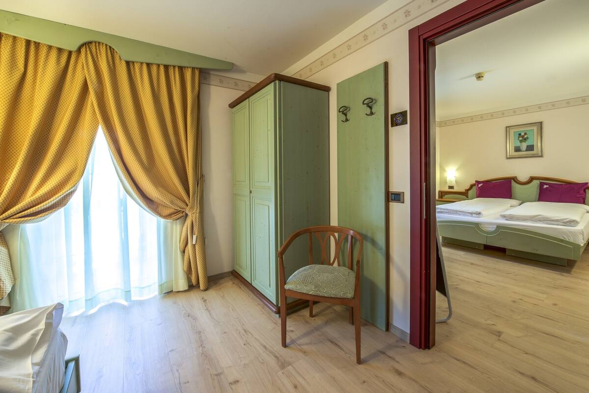A room with a wooden floor, a green wardrobe, a chair, and a bed with a green headboard.
