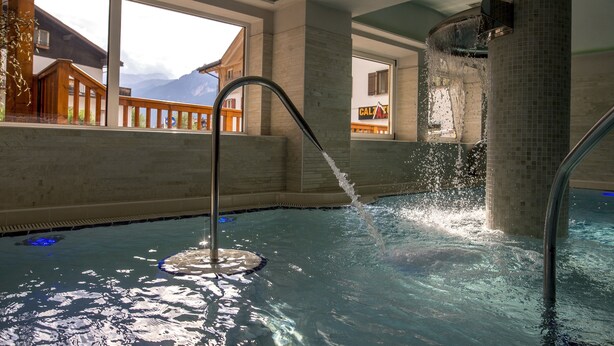 A hot tub with a waterfall feature, large windows, and a view of a mountain. - Albergo Alla Rosa (Canazei)