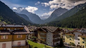 A mountain village with traditional wooden houses, a clear sky, and a valley with mountains in the background. - Albergo Alla Rosa (Canazei)