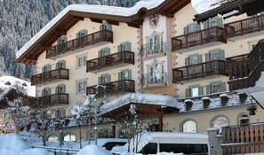 A multi-story hotel with balconies, snow-covered surroundings, and a mountainous backdrop.