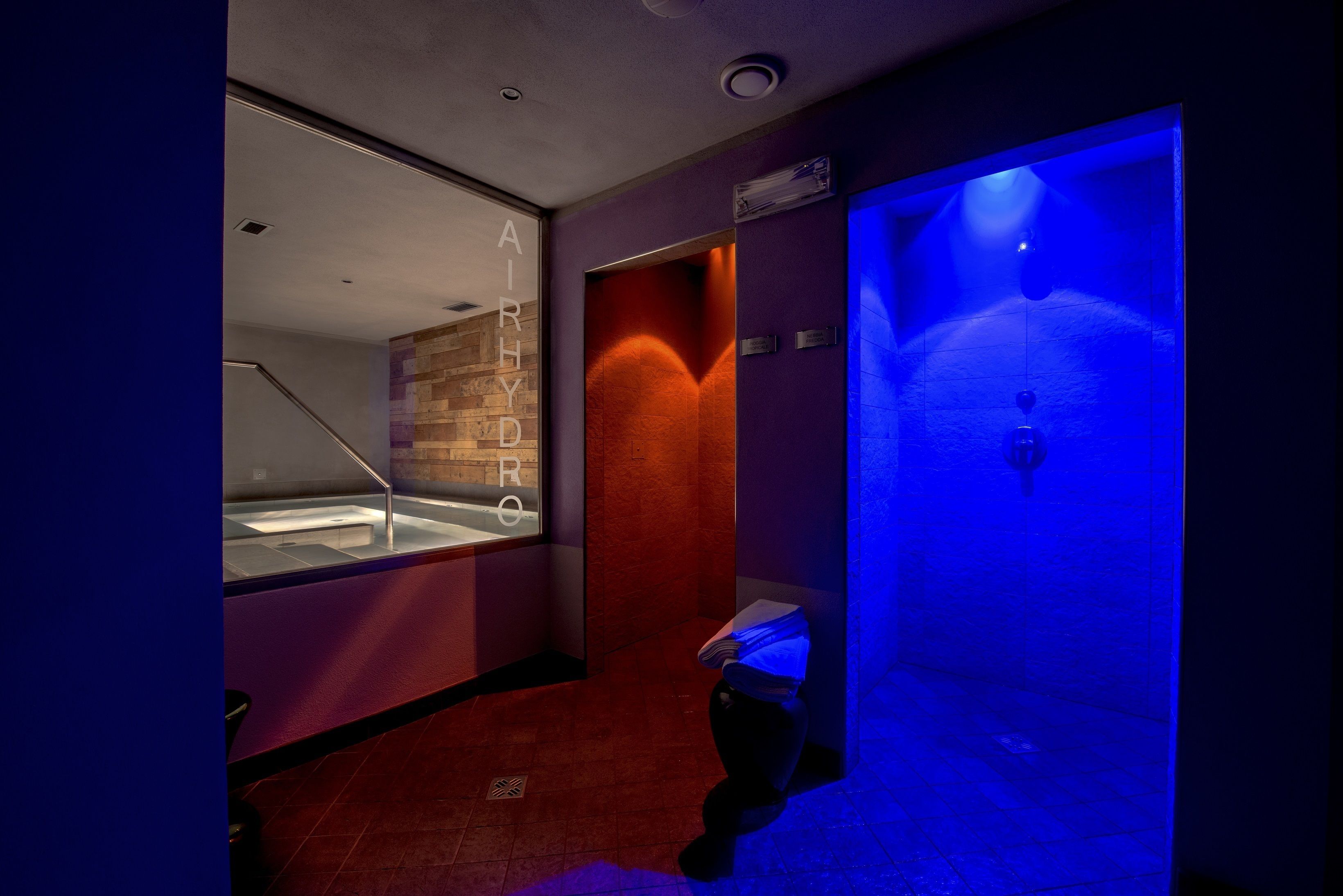 A modern bathroom with a glass-enclosed jacuzzi, a red-tiled floor, and a blue-lit steam room.