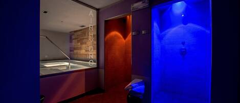 A modern bathroom with a glass-enclosed jacuzzi, a red-tiled floor, and a blue-lit steam room.
