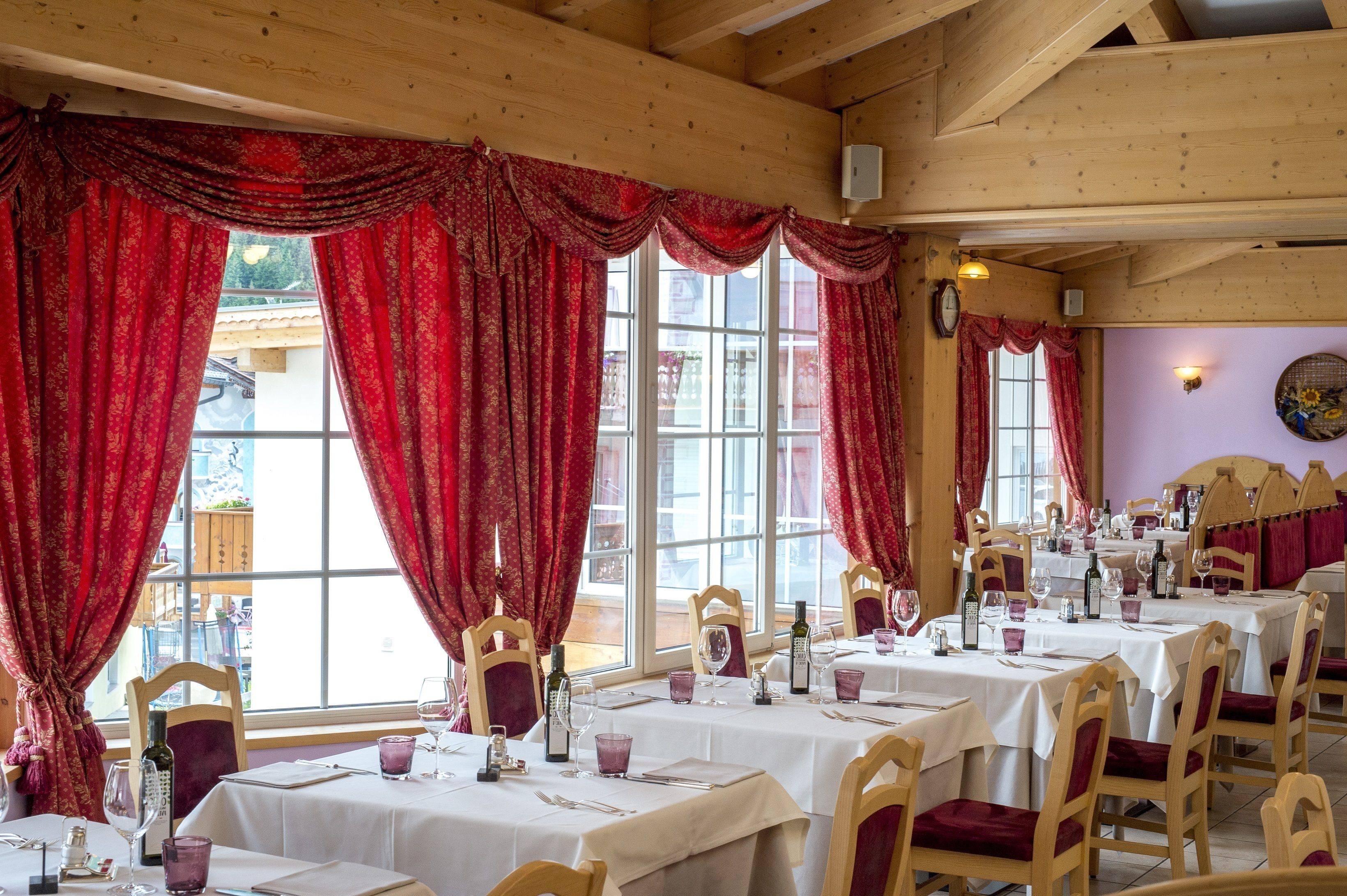 A restaurant with wooden beams, red curtains, and tables set for dining.