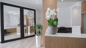 A reception area with a wooden reception desk, a potted plant, and a large mirror reflecting the interior. - Hotel Paradiso (Senigallia)