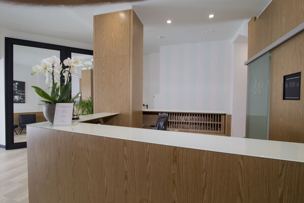 Un mostrador de recepción con detalles de madera, una orquídea en maceta y un certificado enmarcado sobre el mostrador.