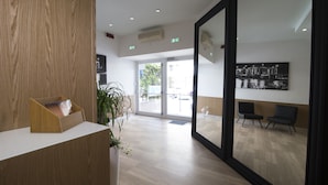 A modern reception area with a wooden reception desk, a potted plant, and a seating area with two chairs. - Hotel Paradiso (Senigallia)