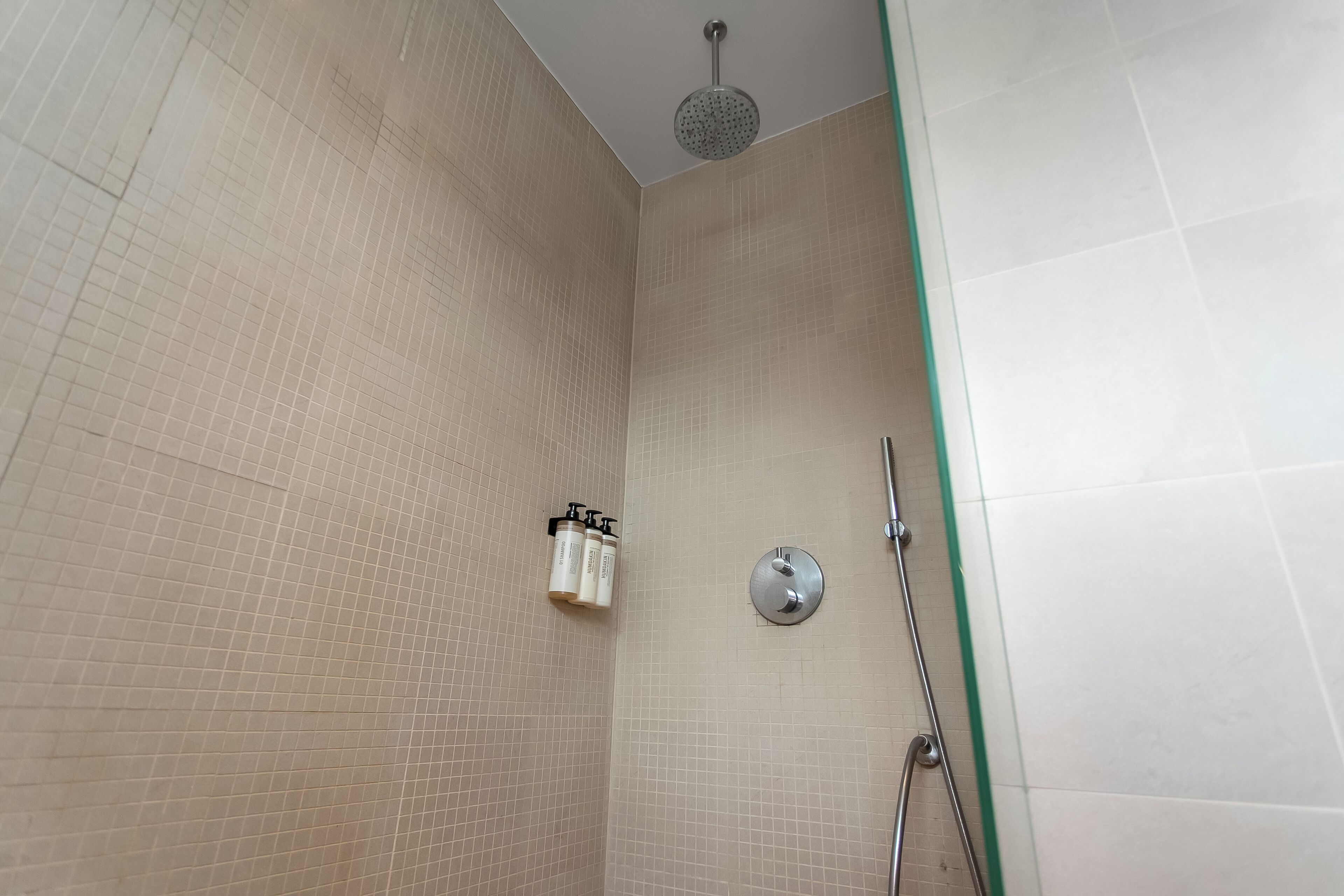 Un espace douche avec des murs carrelés, une douchette à main et un robinet fixé au mur.